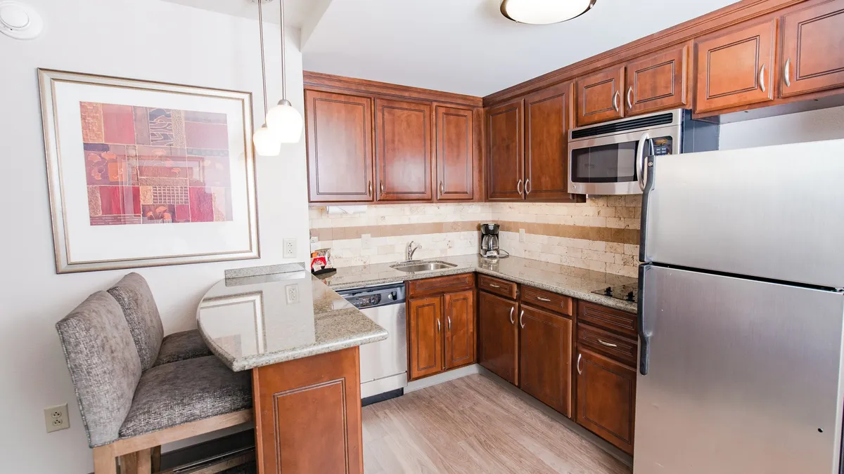 A kitchen and dining area featuring a granite countertop, warm wooden cabinetry, and decorative wall art. The bar seating area is ideal for casual dining or morning coffee, while the ambiance is warm and welcoming—perfect for longer stays and home-like comfort.
