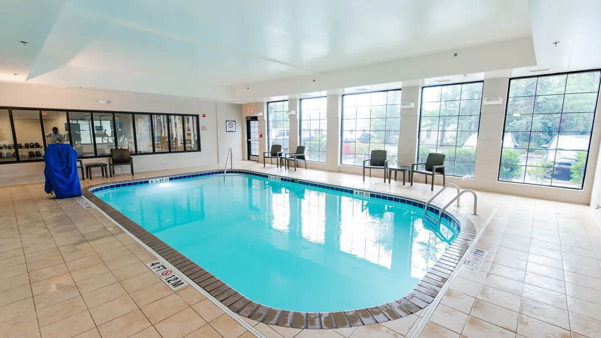 A serene indoor pool area with large windows letting in natural light, a spacious seating area for relaxation, and a tranquil mood. The space is ideal for unwinding after a productive day or socializing with fellow residents.