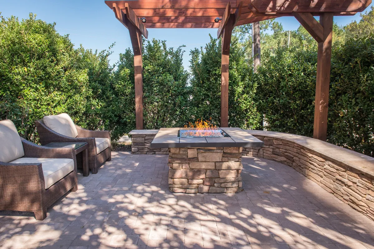 An outdoor seating area featuring a cozy fire pit and pergola is shown in this exterior image. Surrounded by comfortable chairs, the setting transitions smoothly from day to evening with sunset tones, suggesting both relaxation and socializing possibilities.