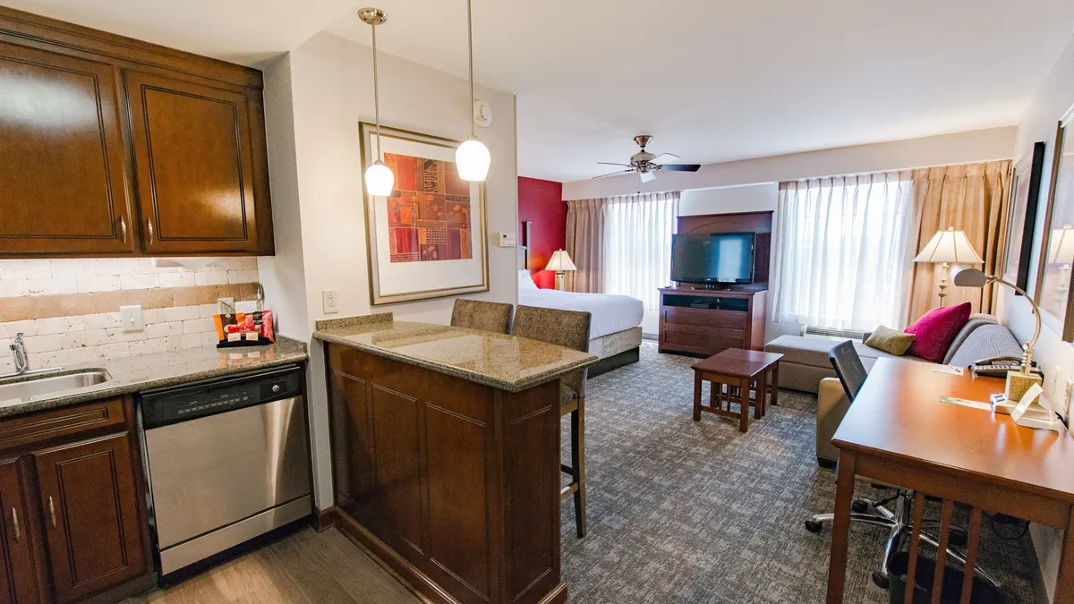 The image showcases a bright, inviting studio with a cozy bed, a compact kitchenette perfectly equipped for easy meals, a dedicated desk area for remote work, and a TV for relaxing entertainment. The space is thoughtfully designed to be both comfortable and functional, making it ideal for couples or solo travelers seeking a versatile home base near Wilmington's top attractions.