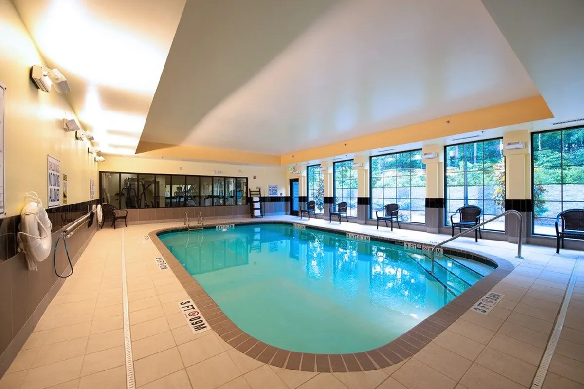 This image captures a tranquil indoor swimming pool area, featuring expansive windows that flood the space with natural light. Comfortable lounge chairs line the pool deck, inviting guests to relax after a swim. The serene atmosphere suggests both morning and evening enjoyment, with hints of socializing and quiet reflection.